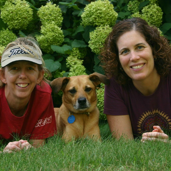 Two women and a dog laying in the grass.